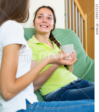 Pair of girlfriends gossiping on sofa Pair of girlfriends gossiping on sofa 19952525