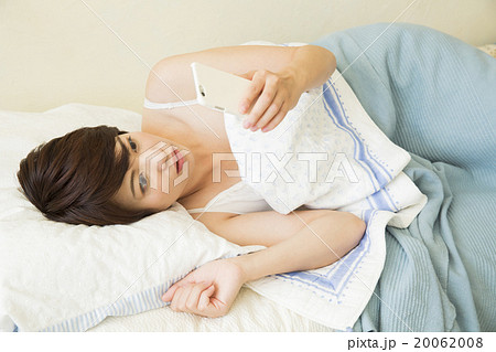 ベッドで寝ながらスマホを操作する若い女性 20062008