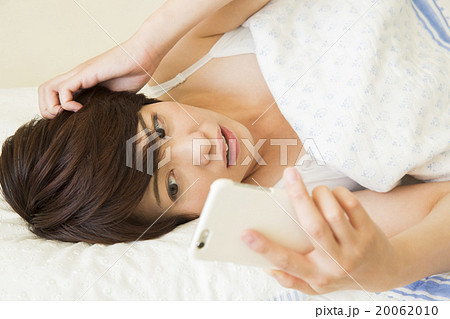 ベッドで寝ながらスマホを操作する若い女性の写真素材 0610