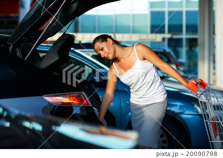 Woman shifts the purchase from shopping cart in the trunk of a c 20090798