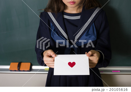 黒板を背に手紙を差し出す女子中高生イメージ 告白 ラブレター 恋愛 イメージ 正面 メインの写真素材