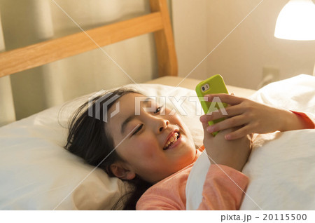 ベッドでスマホを見る女の子の写真素材