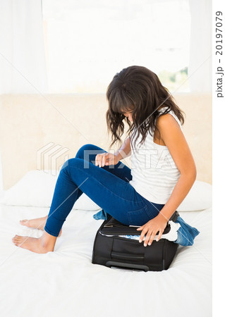 Woman sitting on her overfull suitcase 20197079
