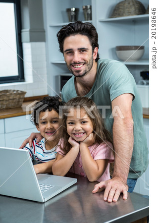 Smiling father using laptop with his children in kitchen 20198646