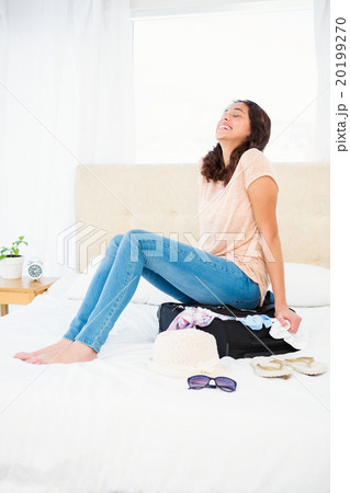 Woman sitting on her overfull suitcase 20199270