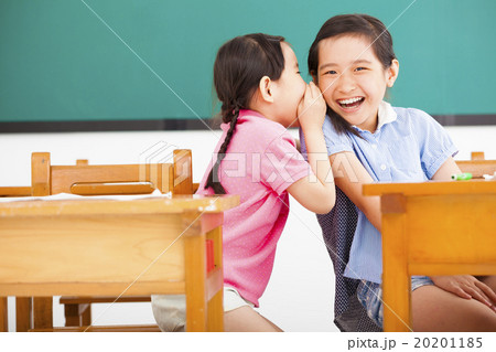 happy little girls whispering and sharing a secret  in classroom 20201185