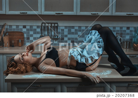 On the kitchen table lies a woman in an apron. 20207368