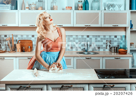 Blonde girl on kitchen kneads dough. 20207426