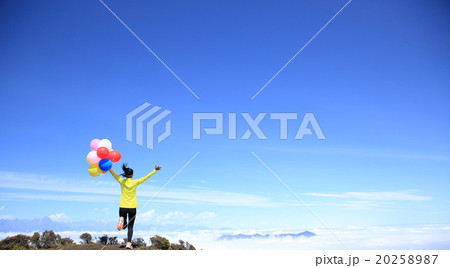 young cheering woman running with colorful balloons on mountain peak 20258987