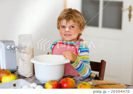 Funny blond kid boy baking apple cake indoors 20304470