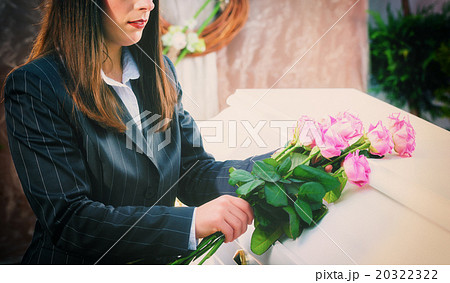 Woman putting rose on coffin at funeral 20322322
