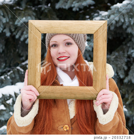 Woman outdoor portrait in wooden photo frame at winter . Snowy weather in fir tree park. 20332718