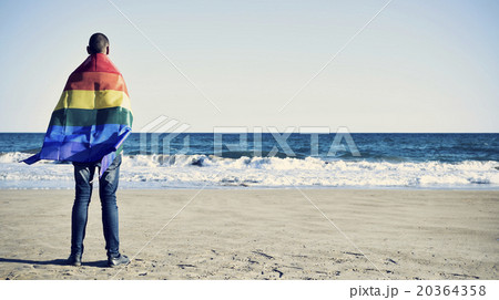 man wrapped in a rainbow flag in front of the sea man wrapped in a rainbow flag in front of the sea 20364358