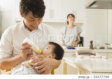 赤ちゃんにミルクを飲ませる若いお父さんの写真素材