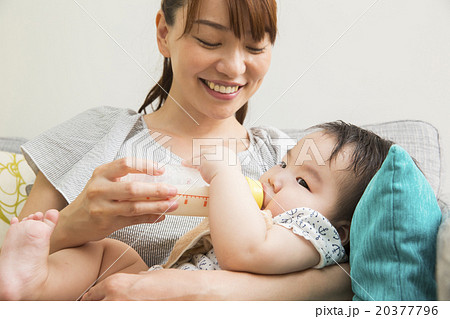 赤ちゃんにミルクを飲ませる若いお母さんの写真素材