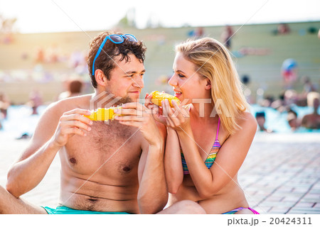 Couple in swimming suits at the pool eating corn 20424311