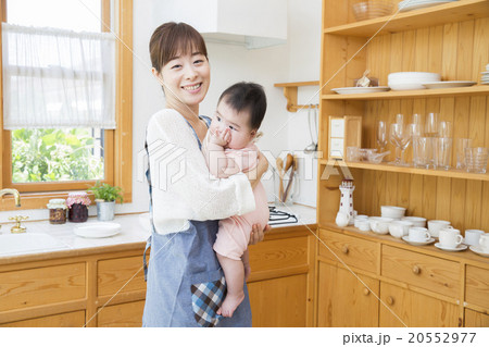 キッチンで赤ちゃんを抱っこするお母さんの写真素材
