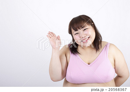 白い背景の前で右手を横に出している笑顔のスポーツブラの太った若い女性 白い背景の前で右手を横に出している笑顔のスポーツブラの太った若い女性 20568367