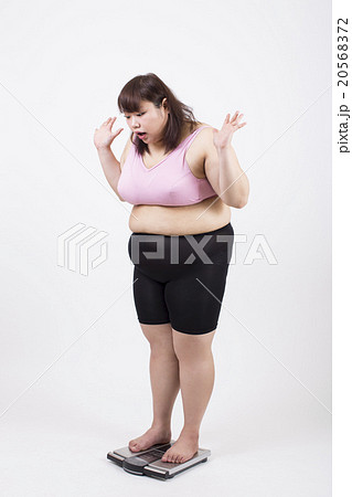 白い背景の前で体重計に乗ってびっくりしている太った若い女性 白い背景の前で体重計に乗ってびっくりしている太った若い女性 20568372