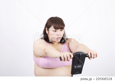 白い背景の前で体脂肪計で体脂肪を計りびっくりしている太った若い女性 白い背景の前で体脂肪計で体脂肪を計りびっくりしている太った若い女性 20568528