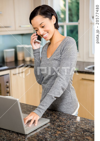 Smiling brunette on a phone call using laptop Smiling brunette on a phone call using laptop 20577480