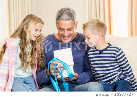 Father opening gift given by children on sofa 20577727