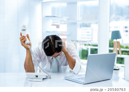 Overwhelmed asian businessman answering the phone 20580763