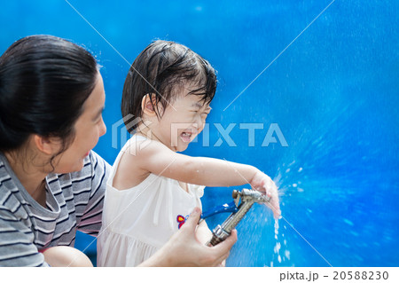 Little asian girl and mother play with water hose Little asian girl and mother play with water hose 20588230