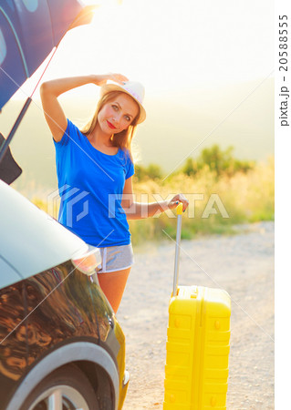 Woman with a yellow suitcase standing near the trunk of a car pa Woman with a yellow suitcase standing near the trunk of a car pa 20588555