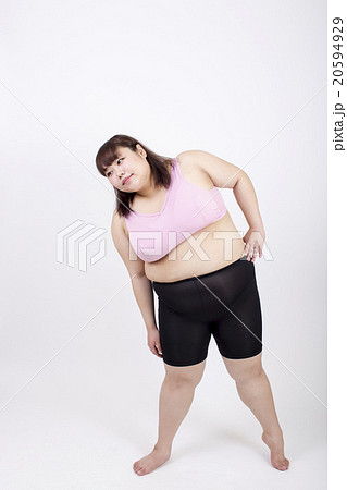 白い背景の前で左手を脇腹にあてストレッチをしている太った若い女性 白い背景の前で左手を脇腹にあてストレッチをしている太った若い女性 20594929