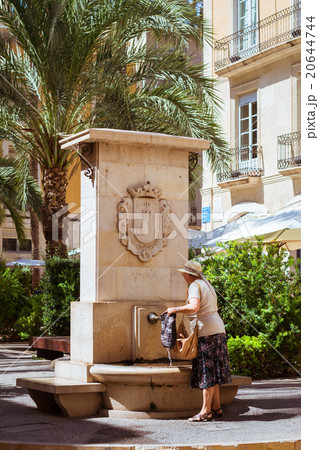Elderly woman collects water in fountain on street 20644744