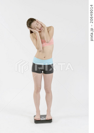 体重計に乗り頭を抱える若い女性 20649014