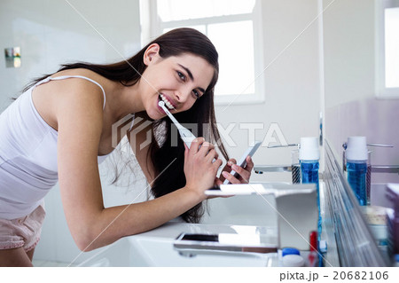 Brunette using smartphone while brushing teeth Brunette using smartphone while brushing teeth 20682106