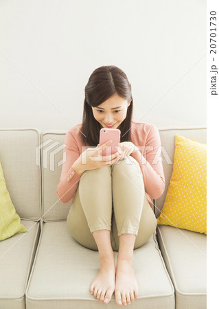 ソファでスマホを操作する若い女性の写真素材