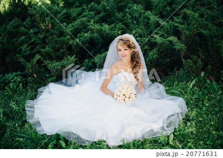 Bride sitting on green grass at park 20771631