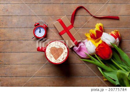 bunch of tulips, red clock, gift and a cup of coffee lying on th 20775784