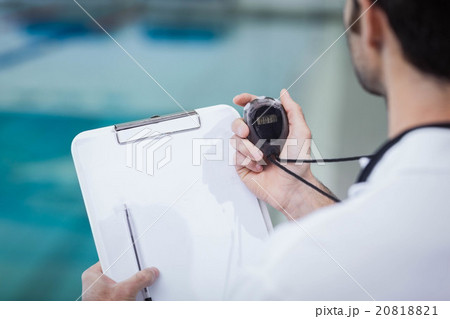 Handsome trainer holding stopwatch and reading clipboard Handsome trainer holding stopwatch and reading clipboard 20818821