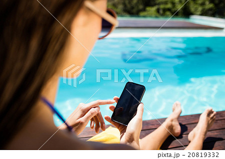 Brunette using smartphone poolside Brunette using smartphone poolside 20819332