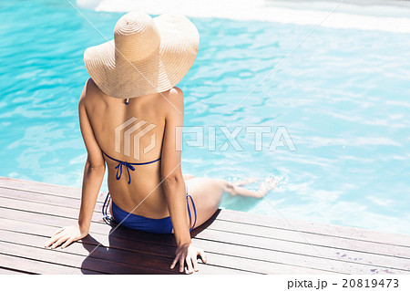 Woman with hat sitting on pools edge 20819473