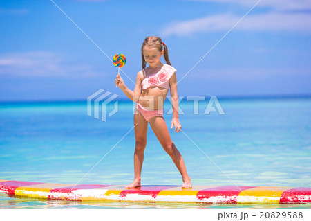 Little girl with lollipop have fun on surfboard in 20829588