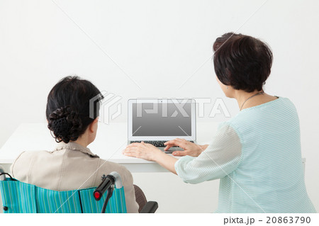ノートPCを操作しているミドル女性と見ている高齢者　介助シーン 20863790