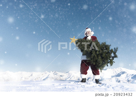 Santa Claus Carrying Christmas Tree on Snow Covered Mountain Santa Claus Carrying Christmas Tree on Snow Covered Mountain 20923432