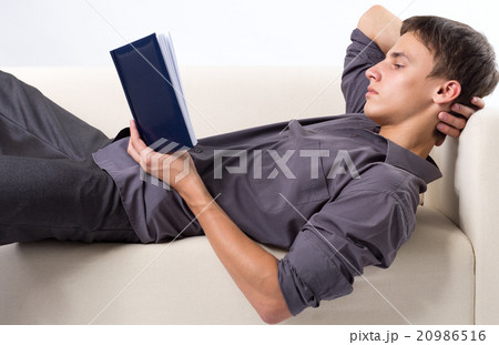Young man reading book while lying at the couch Young man reading book while lying at the couch 20986516