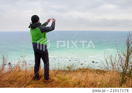 Man in waterproof jacket takes photo of coastline 21017178