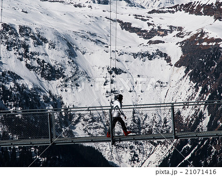 Skier walks on mountain suspension bridge 21071416