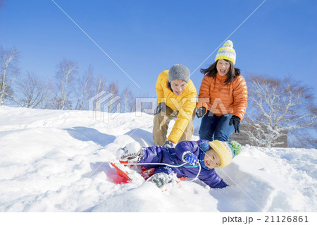 雪の公園でソリ遊びをする3人家族の写真素材