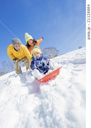 雪の公園でソリ遊びをする3人家族の写真素材