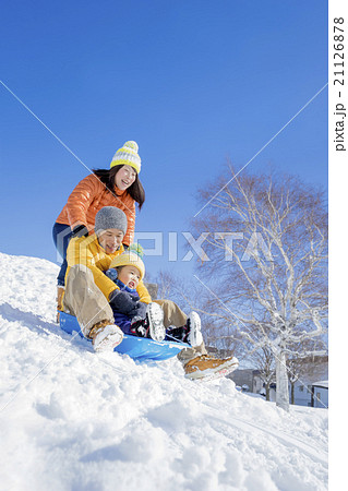 雪の公園でソリ遊びをする3人家族の写真素材
