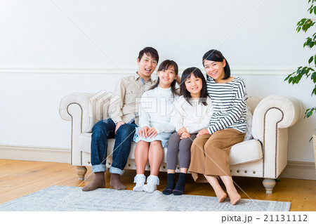 4人家族 仲良し家族 カメラ目線 女の子 女性 男性 父親と母親 娘 ソファーでくつろぐ家族の写真素材