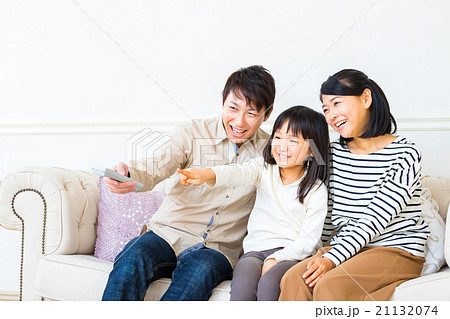 リモコンを持ちテレビを見る3人家族 家族団らん 父親 母親 娘 コピースペース 仲のいい家族の写真素材